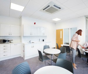 office kitchen in a gloss white design with white breakout tables and grey chairs